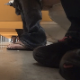 A camera placed under the stall in a public restroom captures multiple women sitting on the toilet including one girl in the next stall with nice tan legs. Over 2 minutes.